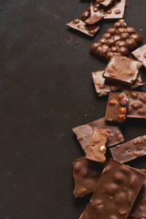 The chunks of broken different chocolate bars with nuts on the black stone surface with space for text. Background with chocolate. Sweet food photo concept.