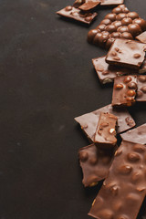 The chunks of broken different chocolate bars with nuts on the black stone surface with space for text. Background with chocolate. Sweet food photo concept.