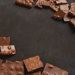 The chunks of broken different chocolate bars with nuts on the black stone surface with space for text. Background with chocolate. Sweet food photo concept.