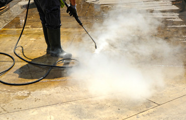 Worker cleaning with pressurized water the pavement of city streets. Covid-19 disinfection