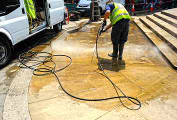 Worker cleaning with pressurized water the pavement of city streets