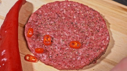 Cook makes meat medallions for burgers. Chef in black food gloves makes cutlet. Cutlets are leveled in steel ring in an even medallion. On top of pouring spices pepper and salt.