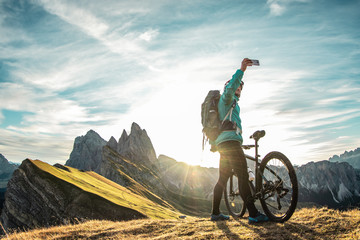 Young man with mountain bike taking selfies on Seceda mountain peak at sunrise. Puez Odle,...