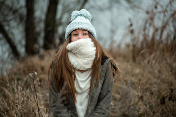 Fototapeta na wymiar Emotion photo. Cute white emotional caucasian teen girl in a blue hat stands in the park in cold autumn weather.