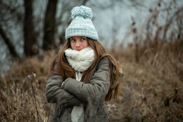 Emotion photo. Cute white emotional caucasian teen girl in a blue hat stands in the park in cold autumn weather.