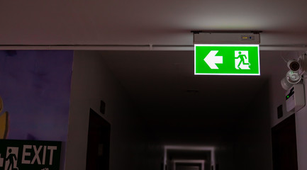 Emergency exit green sign hanging by the ceiling inside a hotel alley