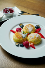 Homemade cheesecakes or Syrniki with jam, fresh fruits and sour cream on a white plate. Ukrainian cuisine. Breakfast food