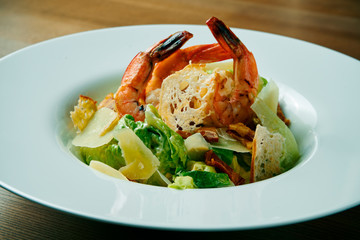 Salad with shrimp, parmesan, lettuce and croutons. Caesar seafood salad in a white bowl on a wooden background. Healthy food and healthy snack. Close up. Selective focus.