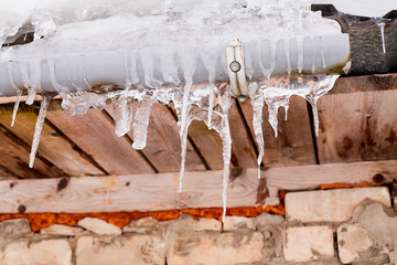 lots of white long icicles on visor of roof of wooden house in spring