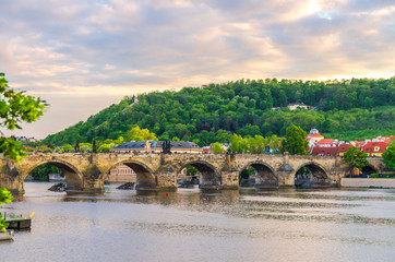 Fototapeta na wymiar Charles Bridge Karluv Most with alley of dramatic baroque statues over Vltava river in Old Town of Prague historical center, garden on slope of Petrin Hill background, Czech Republic, Bohemia, Europe