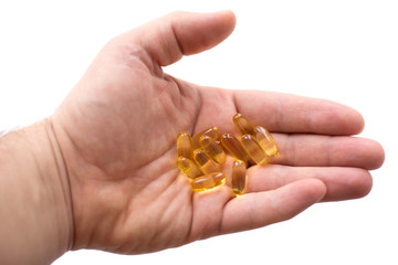 Fototapeta premium A man holds in his hand several fish oil capsules. Omega 3 and vitamin D pills. Healthy lifestyle. Selective focus. Side view.