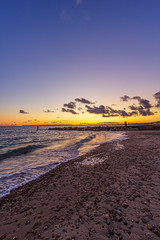 A view of a stony beach at sunset with crashing waves and ecume under a majestic yellow cloudy stormy sky