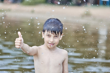a little boy shows a thumbs up like in the middle of frozen water droplets in the air