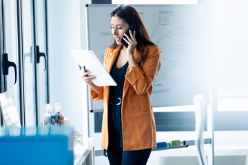 Fototapeta premium Business young woman talking on mobile phone while holding papers in the office.