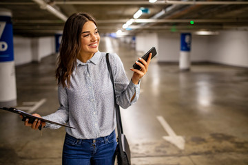 Woman with smart phone in underground parking lot.  Fashionable young woman texting on smartphone....