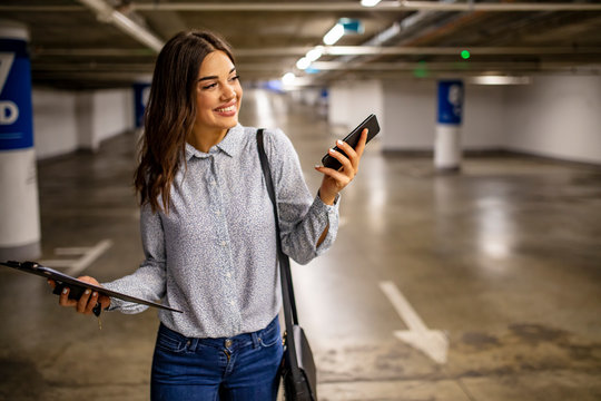 Woman with smart phone in underground parking lot.  Fashionable young woman texting on smartphone. Businesswoman in a parking garage. Woman in the underground car parking