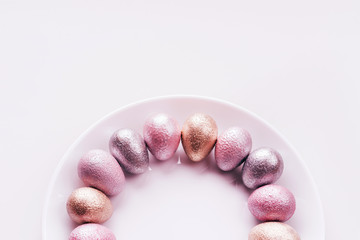 Colored painted pearl chicken and quail eggs of pink, silver, golden color on a purple plate pastel background. Minimalistic creative idea easter festive flat lay. Copyspace for text