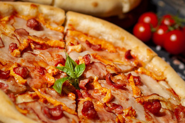 pizza with bacon sausages cheese basil tomatoes cut into pieces on a dark background