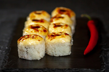 hot sushi rolls with cheese and chili pepper near on a black board close-up