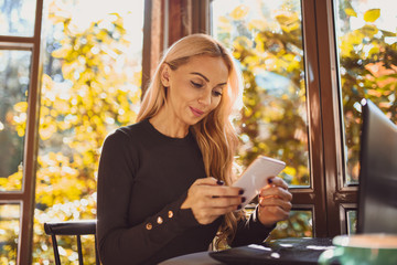 Gorgeous blond woman chatting on her smart-phone by the window in cafe