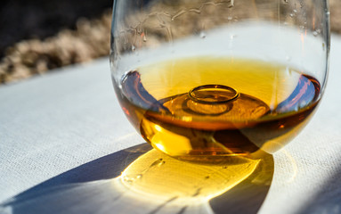 light refracting through a glass of amber colored liquid with a wedding ring at the bottom