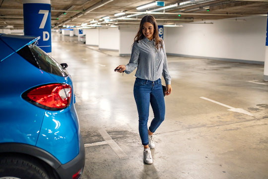Woman in a parking, unlocking in her car. Woman activating her car alarm in an underground parking garage as she walks away. Young business woman walking with car keys in the underground parking.