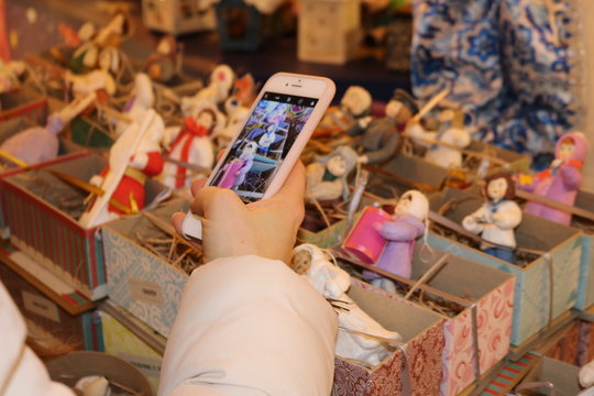 A human hand in a white sleeve holds a white phone over Christmas toys on the store counter and takes pictures of them.