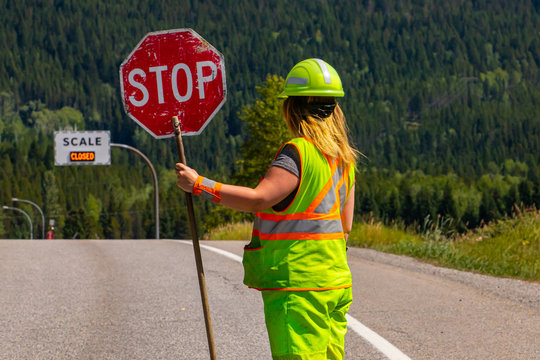 A close up and rear view of a female road construction worker holding a stop stick wearing high visibility safety clothes, roadworks traffic control