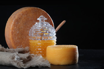 Big round cheese heads on a black background with a jar of honey. Copy space.