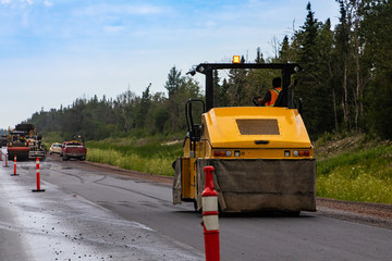 A heavy duty road roller is seen compacting asphalt subsurface during roadworks on a major freeway, transport infrastructure upgrade with copy space