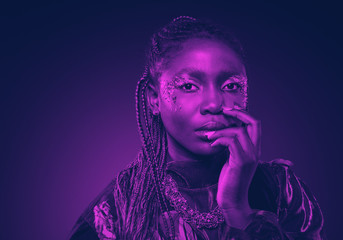 Young African woman with afro hairstyle and golden shiny makeup. Studio shot. Blue and purple duotone neon toning