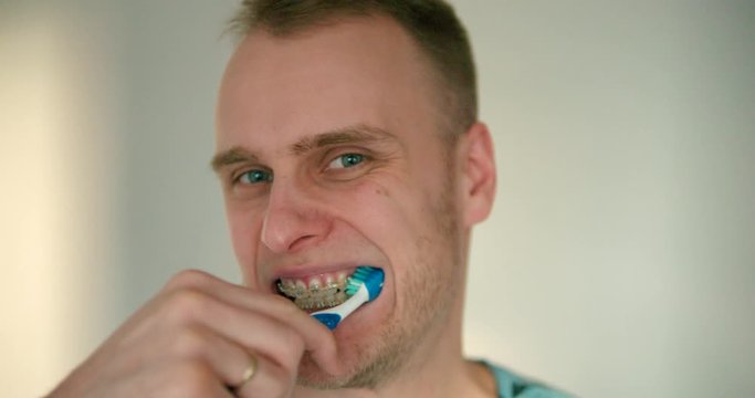 Close up of young man with braces brushing his teeth in slow motion