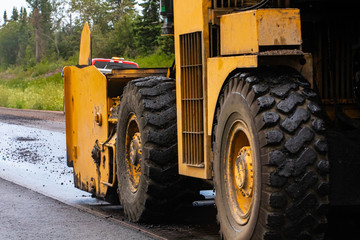 A close up shot on the large wheels and tires of an industrial heavy plant yellow machine used during resurfacing of roads, with copy space on left
