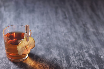 A glass of apple juice with apple chips on a clothespin on a dark background.
