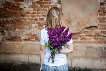 Woman holding a vivid bunch of lilac flowers against brick wall