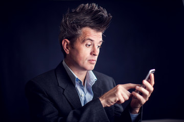 Man with mohawk wearing suit using mobile phone in front of black background.