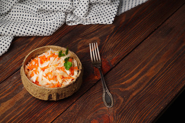 Fermented cabbage with carrots in a ceramic Cup with a sprig of parsley on a wooden, textured background with a fork. Horizontal layout, copy space.