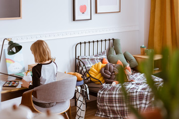 Cute little girl sitting at desk making homework in her stylish vintage bedroom with workspace