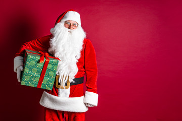 Photo of kind Santa Claus giving xmas present and looking at camera.