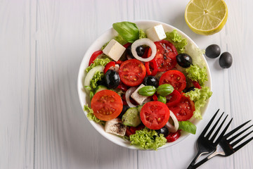 Healthy Greek salad of green lettuce, cherry tomato, onion, pepper, feta cheese, black olives, basil, cucumbers, with olive oil and lemon juice, Top view