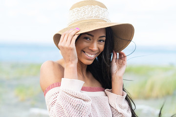 Pretty African American woman wearing floppy hat with a smile at the beach - Powered by Adobe