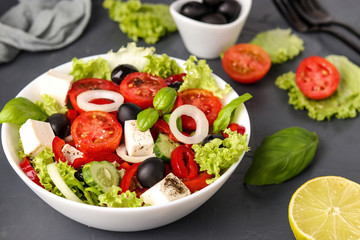 Healthy Greek salad of green lettuce, cherry tomato, onion, pepper, feta cheese, black olives, basil, cucumbers, with olive oil and lemon juice, horizontal orientation
