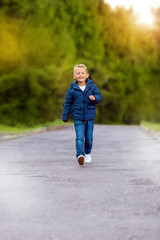Fototapeta premium little boy in a blue jacket runs along the road in the autumn park.