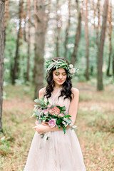 Wonderful brunette smiling bride with the wedding bouquet spending time in the forest. Half-length portrait.