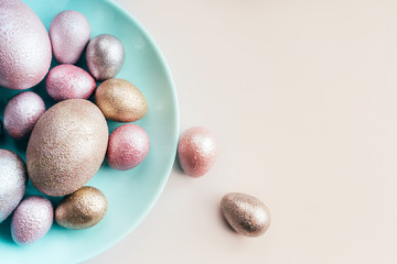 Colored painted pearl chicken and quail eggs of pink, silver, golden color on a blue mint plate pastel background. Minimalistic creative neo easter festive vertical flat lay. Copyspace for text