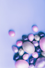 Colored painted pearl chicken and quail eggs pink, silver, golden and blue color on a light blue pastel vertical background. Minimalistic creative classic easter festive flat lay. Copyspace for text