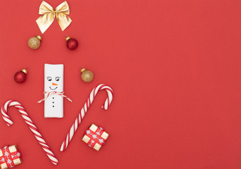 Christmas red background with snowman, candy canes, gift boxes with red ribbon, red and gold balls and gold bow. New Year greeting card. Christmas, New Year concept. Flat lay style with copy space.