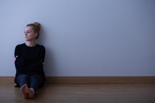 Picture of a sad teenage girl suffering from loneliness, sitting alone on the floor, copy space on empty wall