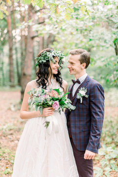 Bride and groom getting married in the forest. Rustic wedding photo. Bride and groom standing on the background of forest, smiling and looking each other
