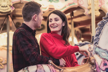 romantic couple taking a moment to kiss while riding horses on carousel